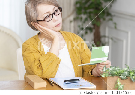 一位老婦人在客廳看著她的臨終遺書和存摺。 133125552