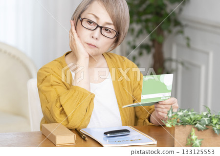 Senior woman looking at her end-of-life note and bankbook in the living room 133125553