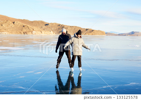 A couple is skating on the frozen Lake Baikal. Transparent ice. A couple is skating on the frozen Lake Baikal. Transparent ice. 133125578
