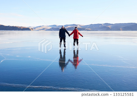 A couple is skating on the frozen Lake Baikal. Transparent ice. A couple is skating on the frozen Lake Baikal. Transparent ice. 133125581