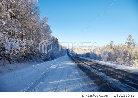 Cars drive along an asphalt road among a snowy winter forest Cars drive along an asphalt road among a snowy winter forest 133125582