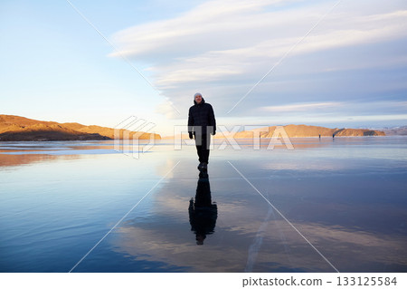 A man walks on the ice of Lake Baikal. A large crack on the transparent ice of the lake. A man walks on the ice of Lake Baikal. A large crack on the transparent ice of the lake. 133125584