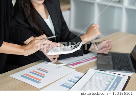 Collaborative Financial Analysis. Businesswomen using calculator and reports for data evaluation. Collaborative Financial Analysis. Businesswomen using calculator and reports for data evaluation. 133126101