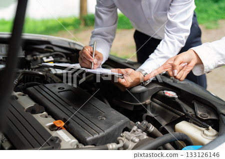 Insurance Assessment. A professional inspecting a car engine while discussing with a client. 133126146