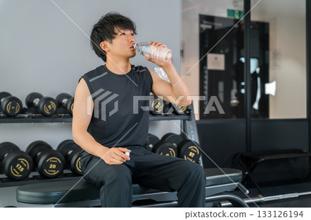 Man drinking water while training/working out at the gym 133126194