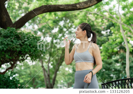 Wellness and Hydration. Young woman drinking water after workout in the park. Wellness and Hydration. Young woman drinking water after workout in the park. 133126205