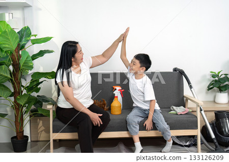 A parent and child share a high-five after completing cleaning tasks, emphasizing teamwork and joy in chores.. 133126209