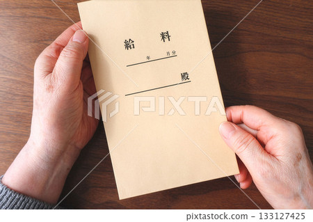 Senior woman's hand holding a pay envelope on a desk 133127425
