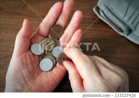 An elderly woman's hand counting coins in her palm and a wallet on a desk 133127428