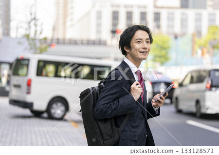 一位手持智慧型手機的商人站在街角 一位手持智慧型手機的商人站在街角 133128571