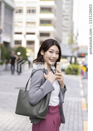 Businesswoman holding a smartphone and smiling while looking at the camera 133128603
