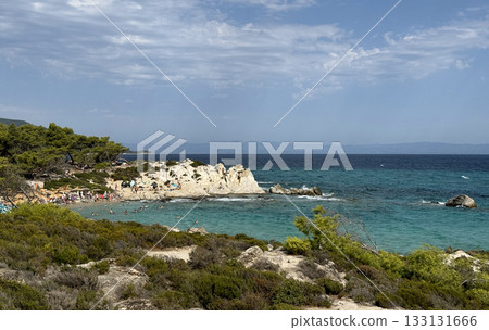 View of Kavourotrypes beach, official nudist beach, Summer sunny day blue sky sea stones, people sunbathing. Sithonia peninsula, Greece View of Kavourotrypes beach, official nudist beach, Summer sunny day blue sky sea stones, people sunbathing. Sithonia peninsula, Greece 133131666