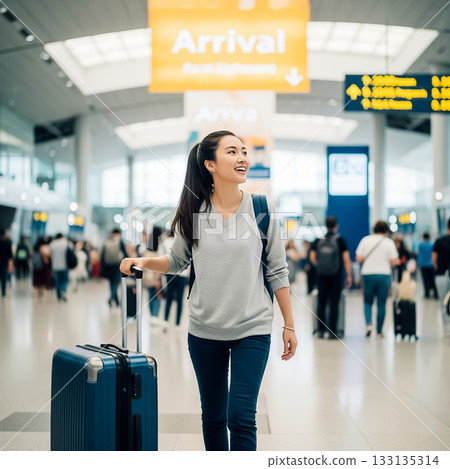 Happy traveler arriving at airport terminal with suitcase in hand during busy daytime 133135314