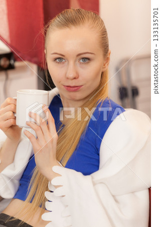 Woman lying on sofa under blanket drinking tea 133135701
