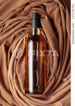 Bottle of white wine against a background of draped beige and brown fabric. 133136781