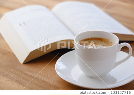 拿著一本打開的書（西洋書）和一個裝有咖啡的咖啡杯，一邊喝咖啡一邊享受閱讀的形象。 133137716