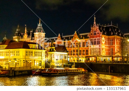 Amsterdam Railway station building. Netherlands at night. Evening street architecture with lights in windows lanterns Amsterdam Railway station building. Netherlands at night. Evening street architecture with lights in windows lanterns 133137961