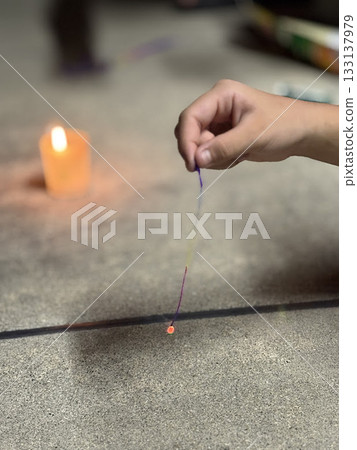 Child's hand lighting incense sticks with candle on a summer day 133137979
