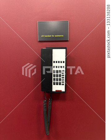 Vertical photo of black telephone on red wall. Concept of landline telephone communication. Warning sign Lift handset for assistance to speak to operator. Quick way to contact operator Vertical photo of black telephone on red wall. Concept of landline telephone communication. Warning sign Lift handset for assistance to speak to operator. Quick way to contact operator 133138208