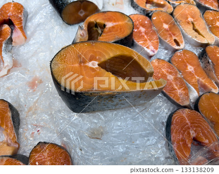 Large salmon steak next to large selection of red fish pieces on ice shelf. Chilled fresh seafood. Natural photo of trout and salmon on counter. Fish corner for buying vitamin rich food 133138209