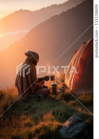 Man drinking tea near tent at mountain sunrise, wrapped in warm clothes and enjoying peaceful solitude, perfect for themes of travel, mindfulness, outdoor living, and morning rituals. 133138689
