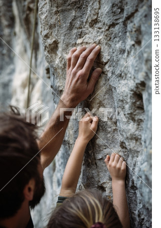Adult and child hands gripping a vertical rock wall in close-up, capturing a climbing lesson and symbolizing support, learning, trust, and outdoor family activities 133138695
