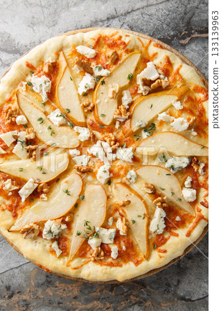 Pear pizza with blue cheese, walnuts, mozzarella and thyme close-up on a wooden board. Vertical top view 133139963