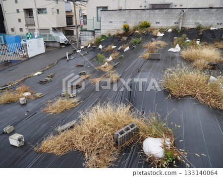 居民區內一個斜坡，上面覆蓋著黑色保護布，雜草叢生。 133140064