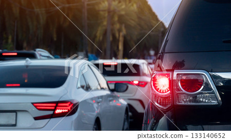 Rear side of luxury car with turn on brake light. Traffic jam on the road with many car queue. Blurred of tall trees for background. 133140652