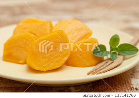 Persimmons, a taste of autumn, served on a plate with sliced persimmons, mint leaves and a fork Persimmons, a taste of autumn, served on a plate with sliced persimmons, mint leaves and a fork 133141760