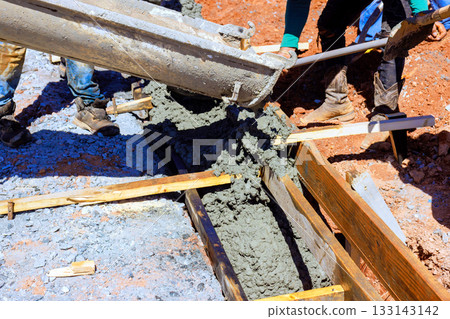 Workers pouring concrete into wooden forms for construction during curbed is concrete Workers pouring concrete into wooden forms for construction during curbed is concrete 133143142