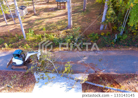 Construction equipment clears fallen tree from pathway in forested area 133143145