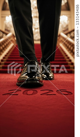 A low-angle view of a person in elegant black patent leather shoes and trousers ascending a grand red carpeted staircase, with the year 2026 etched into the luxurious floor. A low-angle view of a person in elegant black patent leather shoes and trousers ascending a grand red carpeted staircase, with the year 2026 etched into the luxurious floor. 133143486