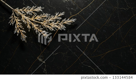 An elegant golden branch featuring intricate clear crystal leaves is artfully arranged on a luxurious black marble background with shimmering golden veining, captured from a top-down perspective. 133144584