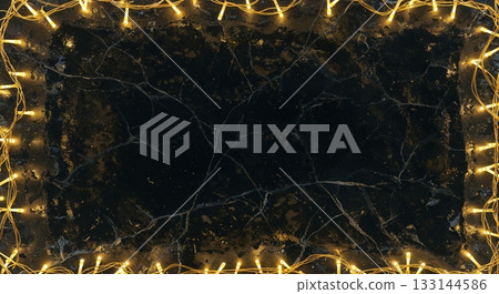Glowing golden string lights form a rectangular frame around a dark, cracked marble surface, creating an elegant backdrop with ample copy space. 133144586