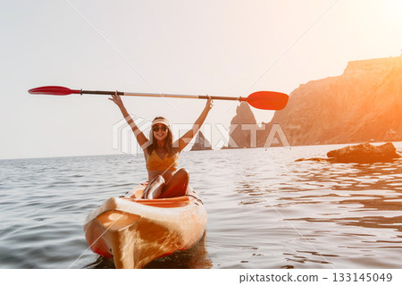 Kayaking Woman Ocean Adventure: Happy woman paddles kayak on calm water with rocky cliffs in the background. Kayaking Woman Ocean Adventure: Happy woman paddles kayak on calm water with rocky cliffs in the background. 133145049