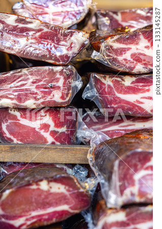Vacuum-sealed cured meat pieces form layered stacks with rich marbling and deep color. market display shows texture, freshness and artisanal quality of traditional delicacy 133145287