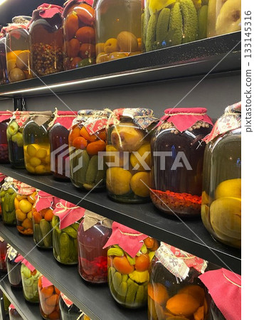 Preserved fruits and vegetables in big jars lined up on black wooden shelves Preserved fruits and vegetables in big jars lined up on black wooden shelves 133145316