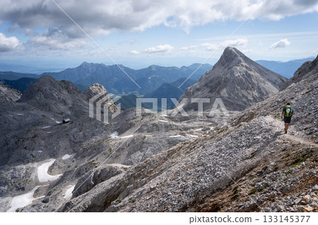 Hiker walking through dry alpine landscape with rocky peaks and no foliage, Slovenia 133145377