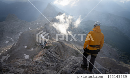 Hiker standing on top of a mountain looking down on beautiful alpine landscape below, Slovenia Hiker standing on top of a mountain looking down on beautiful alpine landscape below, Slovenia 133145389