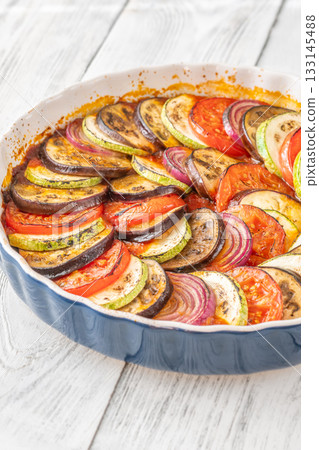 Round baking pot filled with circularly arranged baked vegetable ratatouille 133145488