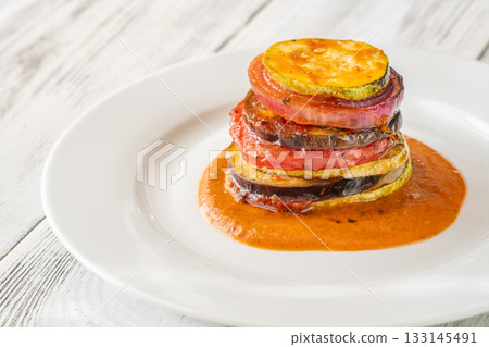 Elegant vertical ratatouille tower layered with colorful vegetables on white plate Elegant vertical ratatouille tower layered with colorful vegetables on white plate 133145491