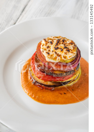 Elegant vertical ratatouille tower layered with colorful vegetables on white plate 133145492