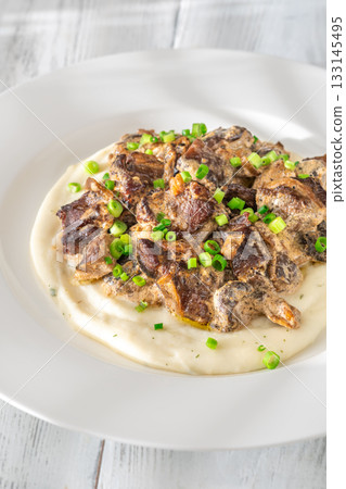 Braised meat and mushroom topping over creamy mashed potato served on white plate 133145495