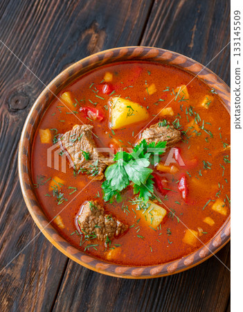 Rustic clay bowl filled with traditional Hungarian Bogracs stew on wooden table Rustic clay bowl filled with traditional Hungarian Bogracs stew on wooden table 133145509
