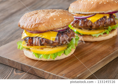Two cheeseburgers with bacon and yellow tomato slices on rustic wooden board Two cheeseburgers with bacon and yellow tomato slices on rustic wooden board 133145516