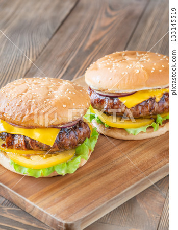 Two cheeseburgers with bacon and yellow tomato slices on rustic wooden board 133145519