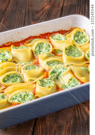 Golden baked lumaconi filled with ricotta and spinach resting in rich tomato sauce 133145544