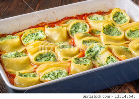 Golden baked lumaconi filled with ricotta and spinach resting in rich tomato sauce Golden baked lumaconi filled with ricotta and spinach resting in rich tomato sauce 133145545