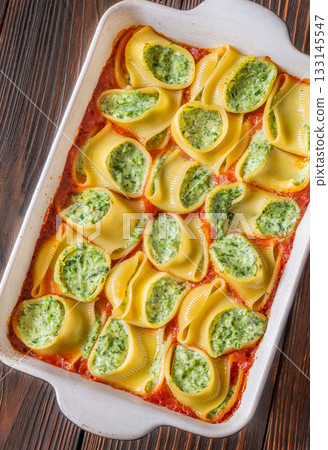 Golden baked lumaconi filled with ricotta and spinach resting in rich tomato sauce 133145547